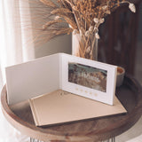 Hands holding the Our Wedding Video Book open, displaying wedding footage on the built-in screen